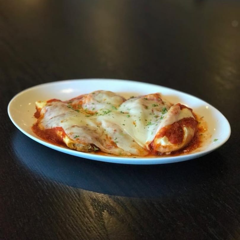 Baked manicotti pasta with melted mozzarella cheese, marinara sauce, and parsley on a white oval plate.