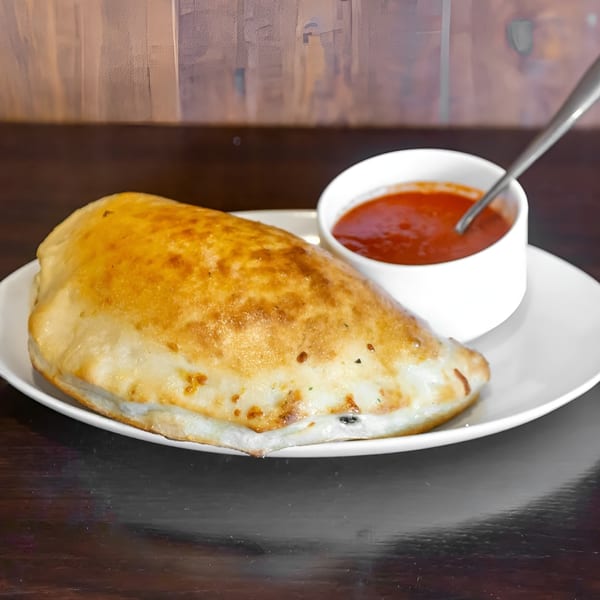 Golden-brown calzone on a white plate with a side of red marinara sauce and a spoon.