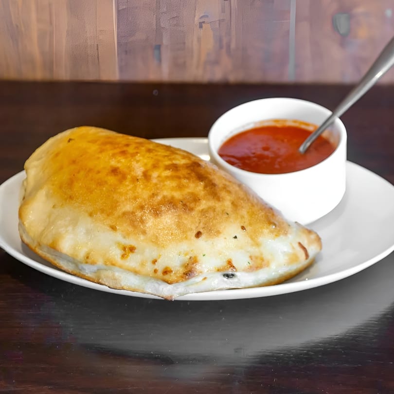 Golden-brown calzone on a white plate with a side of red marinara sauce and a spoon.