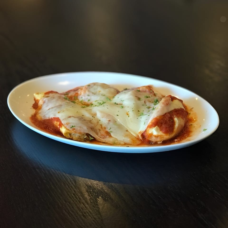 Four cheese-covered manicotti in red sauce, garnished with parsley, on a white oval plate.