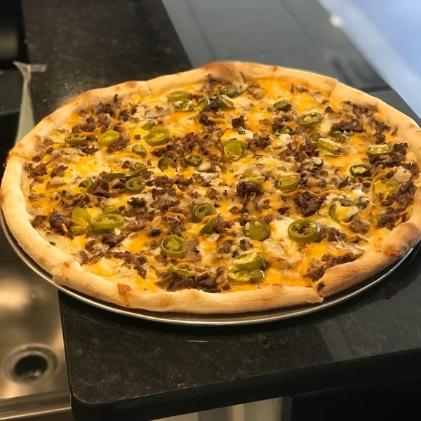 A whole pizza with ground meat, melted cheese, and sliced green jalapeños on a metal tray.