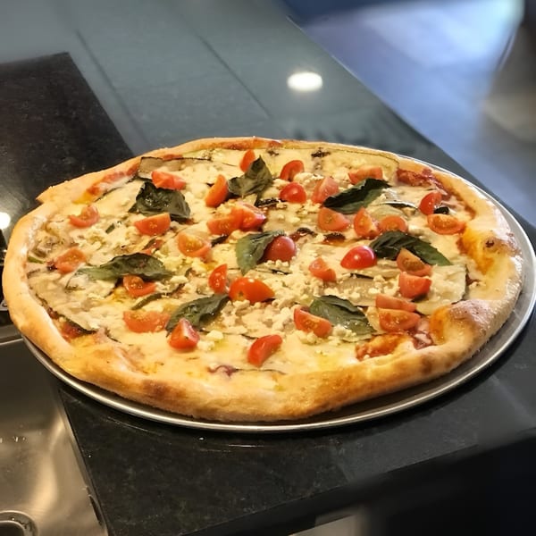 Freshly baked pizza with cherry tomatoes, basil, and feta cheese on a dark countertop.